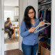 Woman looking at empty hangers in closet while man drinks coffee at table nearby.