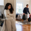 Woman watching man preparing garbage bags in the living room from the kitchen doorway.