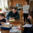 Cal writes minutes on a legal pad at the kitchen table while Ivy stands nearby, uneasy, as the kids sit with notebooks.
