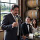 A man mid-toast freezes as he stares at a place card, with the smiling groom and tense bride behind him.