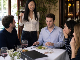 Mara stands to toast while sliding a binder toward stunned friends as Evan turns pale.