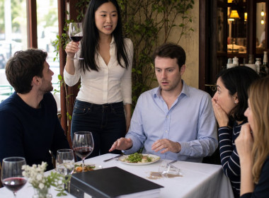 Mara stands to toast while sliding a binder toward stunned friends as Evan turns pale.