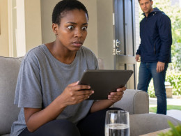Mara stares at a tablet on the couch as Evan walks in through the front door.
