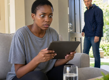 Mara stares at a tablet on the couch as Evan walks in through the front door.