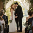 At the altar, the redheaded bride stands tense as the groom leans in smiling, gripping her hand too tightly while the officiant looks startled.