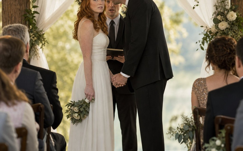 At the altar, the redheaded bride stands tense as the groom leans in smiling, gripping her hand too tightly while the officiant looks startled.
