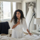 Bride in a satin robe clutches a phone, stunned, beside an unmade bed with a suit jacket nearby.