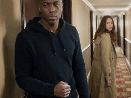 A tense young man stands by a hotel room door as a woman rounds the corner and freezes.