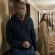 A tense young man stands by a hotel room door as a woman rounds the corner and freezes.