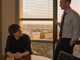 After-hours in a glass-walled conference room, Graham lowers the blinds while Iris looks up from the table, tense.