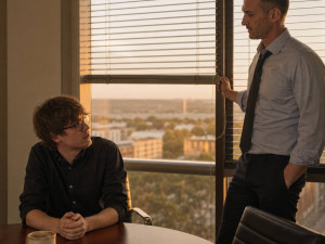 After-hours in a glass-walled conference room, Graham lowers the blinds while Iris looks up from the table, tense.