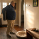 A heavyset gray-haired man with glasses stares at an empty leash hook beside a flattened dog bed.