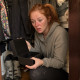A red-ponytailed woman crouches in a closet holding an open lockbox, shocked.