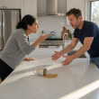 Maren confronts Caleb across the kitchen island as he reaches toward the phone, coffee spilled nearby.