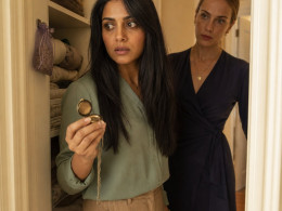 A woman clutches an open locket in a linen closet as a blonde woman with a scarred eyebrow watches from the doorway.
