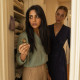 A woman clutches an open locket in a linen closet as a blonde woman with a scarred eyebrow watches from the doorway.
