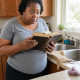 Iris in her kitchen holding open a Bible as a pawn ticket slips out, her face tense with shock.